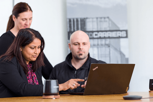 Three professionals collaborating at a table, focused on a laptop screen during a meeting.